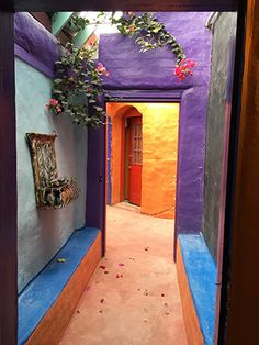 an alley way with purple walls and flowers on the wall, painted in bright colors