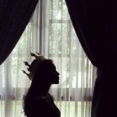 a woman standing in front of a window wearing a crown