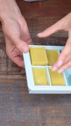 two hands reaching for some food in a small tray on a wooden table with one hand touching another's finger