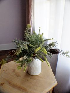 a white vase filled with pine cones on top of a wooden table