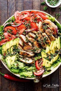 chicken salad with avocado and tomatoes in a bowl on top of a wooden table