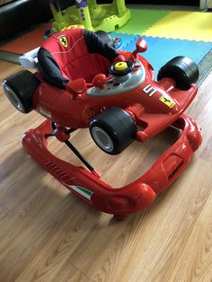 a red toy car sitting on top of a wooden floor next to a child's play table