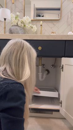 a blonde woman is opening the cabinet in her bathroom with white flowers on the counter