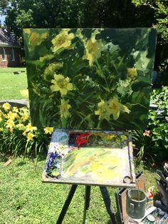 an easel sitting in the grass with flowers painted on it