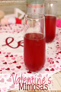 two glasses filled with red liquid sitting on top of a pink table cloth next to each other