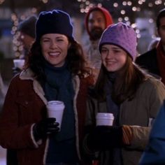 two women standing next to each other holding coffee cups