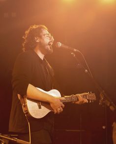 a man holding a guitar while standing in front of a microphone and singing into a microphone