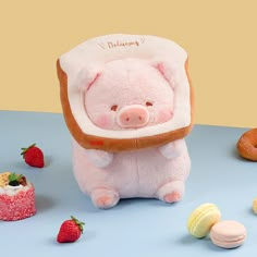 a pink stuffed pig sitting on top of a table next to doughnuts and strawberries