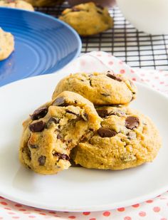 three chocolate chip cookies on a white plate next to a blue plate with red polka dots