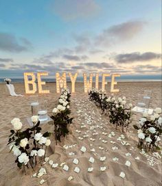 a beach wedding setup with flowers on the sand and be my wife written in large letters