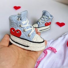 a hand is holding two crocheted shoes with hearts on them