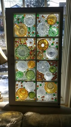 a window with many different colored glass plates on it in front of a couch next to a window