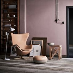 an egg chair and ottoman in front of a pink wall with pictures on the floor