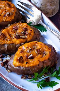 baked sweet potatoes topped with pecans and chopped parsley on a plate next to a fork