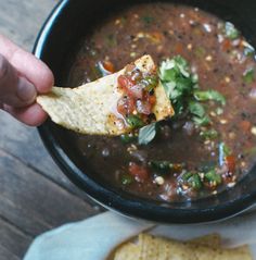 a person dipping tortilla chips into a bowl of black bean soup