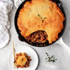 a skillet filled with meat and cheese next to a white plate full of food