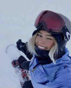 a woman sitting in the snow with her skis and goggles on, smiling at the camera