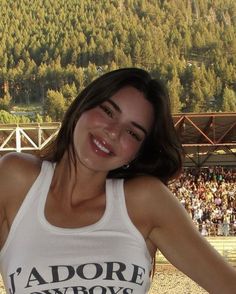 a woman standing in front of a crowd wearing a white tank top with the words l'adore cowboys on it