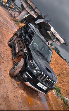 a black truck parked on the side of a dirt road next to a building and water