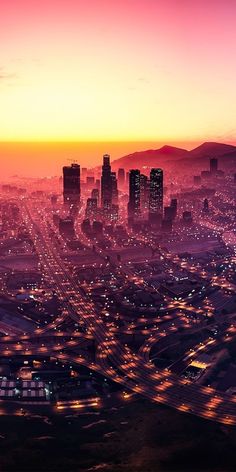 an aerial view of a city at night with the sun setting in the distance and cars driving on the road