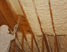 a person spray painting the ceiling in a room that is under construction with wood beams