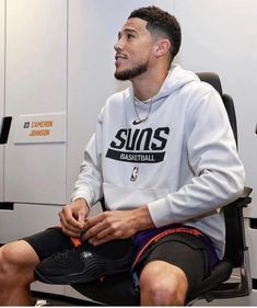 a man sitting on top of a chair wearing a white sweatshirt and black shorts with the sun's basketball logo on it