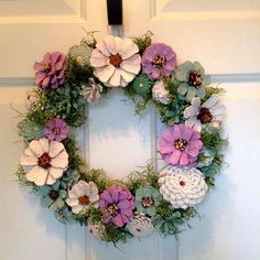 a wreath with flowers and pine cones hanging on the front door to decorate it for someone's special occasion