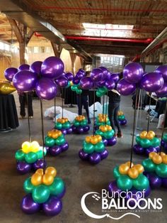 purple and green balloons are arranged on sticks in the middle of an indoor event area