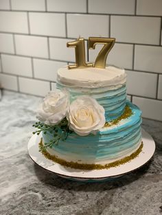 a blue cake with white flowers and the number seven on top is sitting on a counter