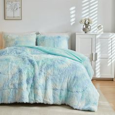 a bed with blue and white comforters in a bedroom next to a dresser,