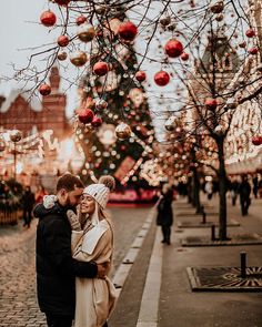 a man and woman standing next to each other in front of a tree with christmas decorations