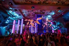 a large group of people standing around in a room with lights and decorations on the ceiling