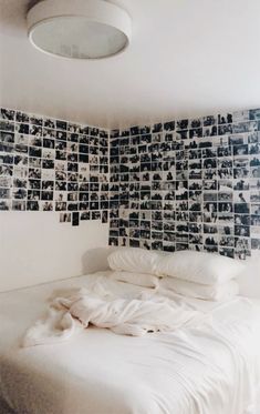 a white bed sitting under a light next to a wall with pictures on the walls