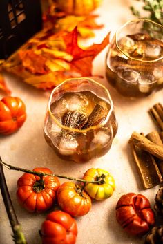 two glasses filled with liquid sitting on top of a table next to autumn leaves and pumpkins