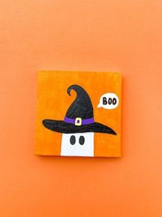 an orange square with a black witches hat on it, and the word boo spelled out