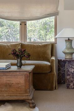 a living room with a couch, coffee table and lamp in front of a window