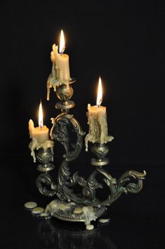 three candles are lit in an ornate metal candle holder on a black background stock photo