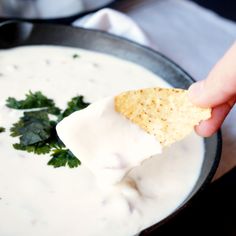 a person dipping tortilla chips into a bowl of white sauce with cilantro