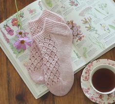 a cup of tea and two pink socks on a table next to an open book