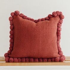 a red pillow with pom - poms on it sitting on top of a wooden table