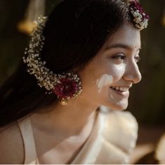 a woman with flowers in her hair smiles at the camera while she is wearing a white dress