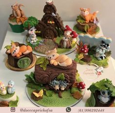 a table topped with lots of cakes covered in fondant animals and trees on top of green leaves