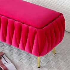 a pink bench sitting on top of a carpeted floor next to a white bed