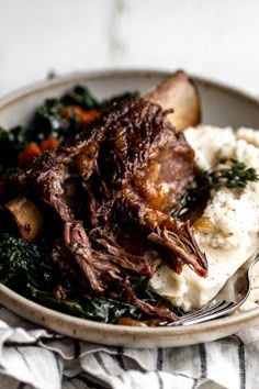 a plate with meat, mashed potatoes and spinach on it next to a fork