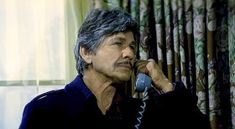 a man talking on a phone in front of curtains