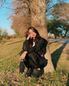 a woman sitting on the ground in front of a tree with her hands to her face