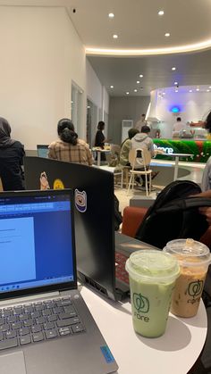 two laptops are sitting on a table with coffee cups and people in the background