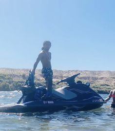 a man standing on top of a jet ski in the water next to a woman