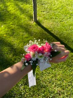 a woman's hand holding a bouquet of pink and white flowers in the grass