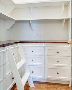 an empty kitchen with white cabinets and shelves on the wall, next to a step ladder